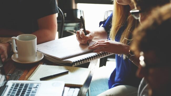 A diverse team discussing ideas around a table with notes and laptops. — sell your course successfully