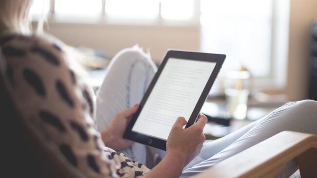 A person sitting comfortably while reading an ebook on a tablet.
